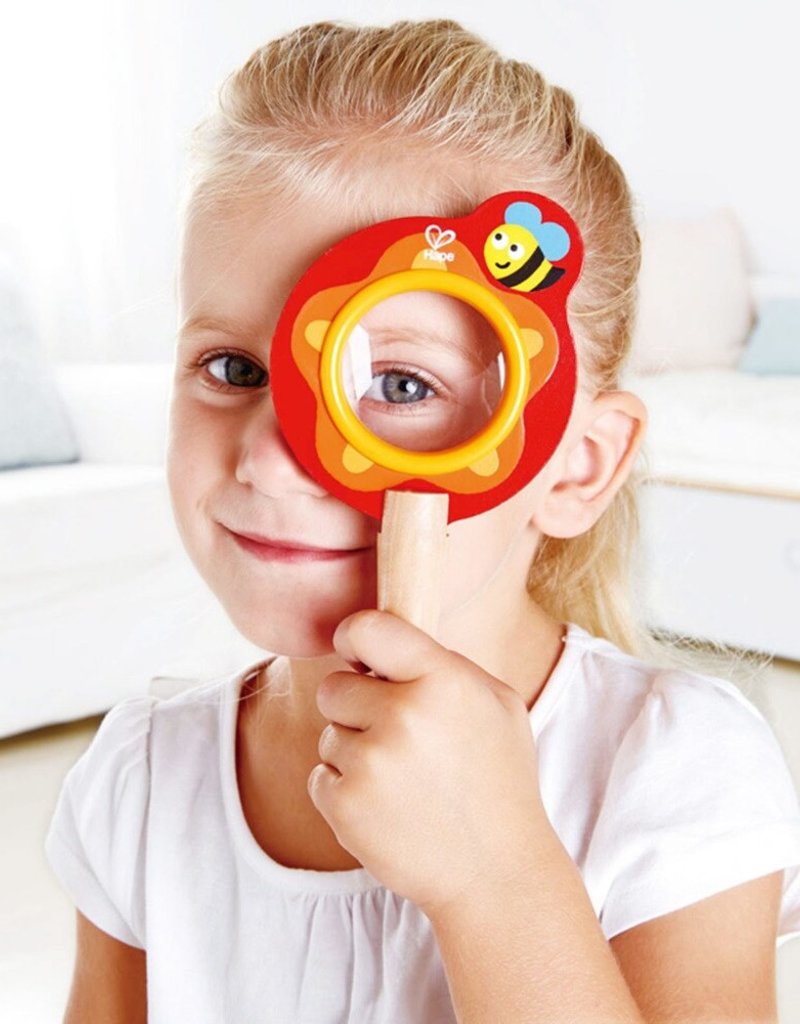 A child is looking through the wooden Hape bee magnifying glass. 